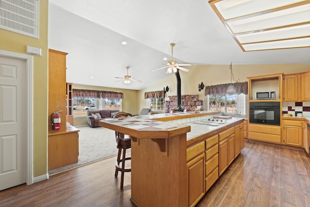 kitchen featuring tile counters, lofted ceiling, stainless steel microwave, a wood stove, and black oven