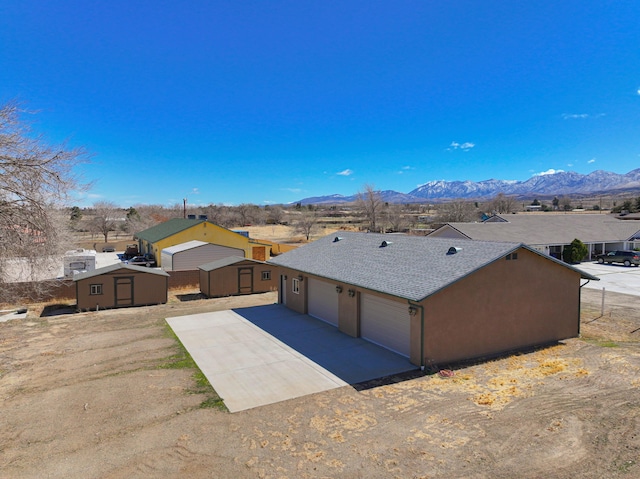 view of front of home featuring a shingled roof, an outbuilding, a storage unit, a mountain view, and stucco siding