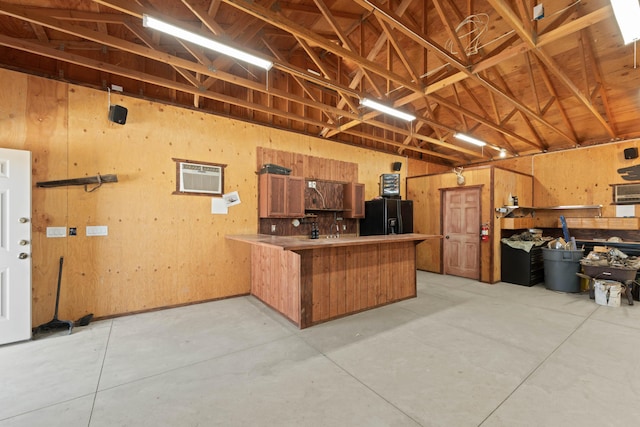 garage featuring an AC wall unit, black fridge with ice dispenser, and wood walls