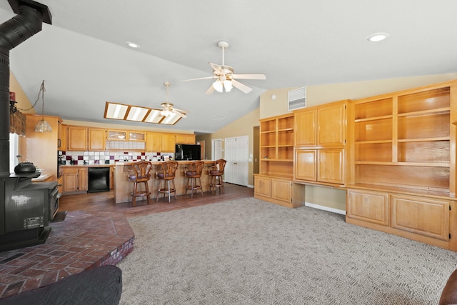 living area with a wood stove, a ceiling fan, vaulted ceiling, and built in desk