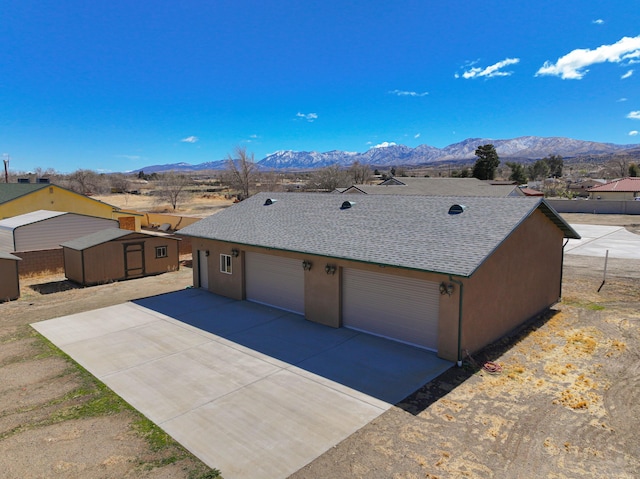 view of front of house featuring a garage, a storage shed, an outdoor structure, a mountain view, and stucco siding