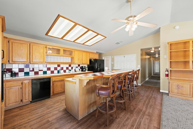 kitchen featuring visible vents, tile counters, a kitchen island, a breakfast bar, and black appliances