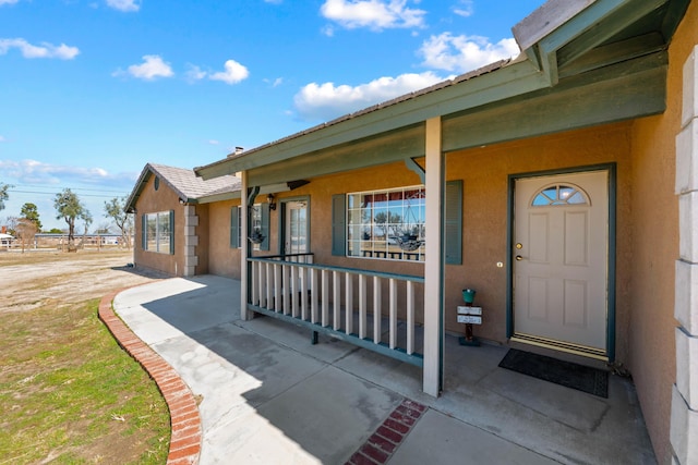 view of exterior entry with covered porch and stucco siding