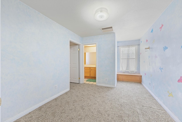 unfurnished bedroom featuring visible vents, ensuite bathroom, attic access, light carpet, and baseboards