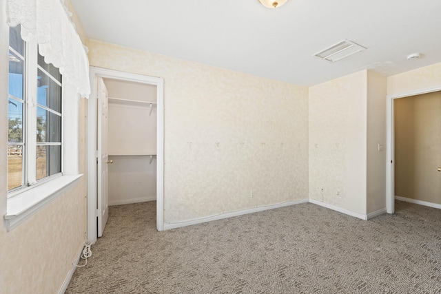 unfurnished bedroom with baseboards, visible vents, a walk in closet, carpet flooring, and a closet