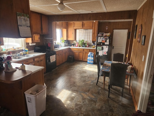 kitchen with sink, a paneled ceiling, wood walls, and black appliances