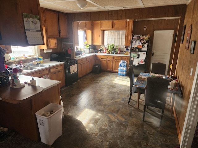 kitchen with sink, a paneled ceiling, fridge, wood walls, and black range with gas cooktop