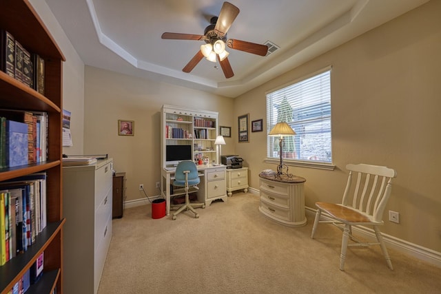 carpeted home office with a raised ceiling and ceiling fan