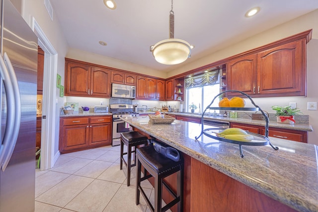 kitchen featuring light stone counters, light tile patterned floors, appliances with stainless steel finishes, a kitchen breakfast bar, and pendant lighting