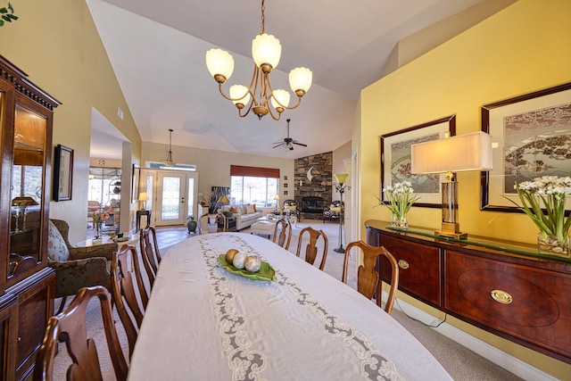 carpeted dining space featuring a stone fireplace, ceiling fan with notable chandelier, and lofted ceiling