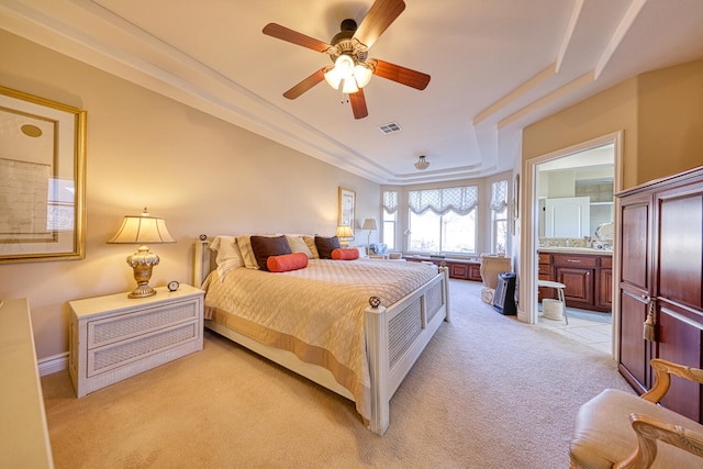 bedroom with light carpet, connected bathroom, a tray ceiling, and ceiling fan