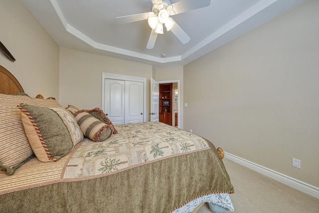 bedroom with ceiling fan, carpet flooring, a tray ceiling, and a closet