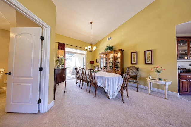 carpeted dining space featuring high vaulted ceiling and an inviting chandelier