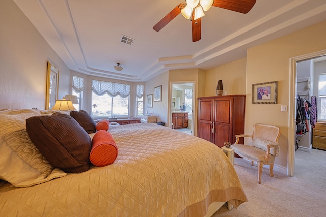 carpeted bedroom featuring a raised ceiling, a walk in closet, ceiling fan, and ensuite bath