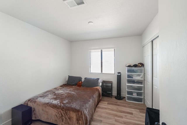 bedroom with a textured ceiling, a closet, visible vents, and wood finished floors