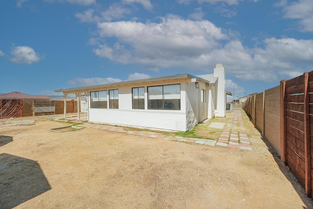 rear view of property with fence, a chimney, and stucco siding