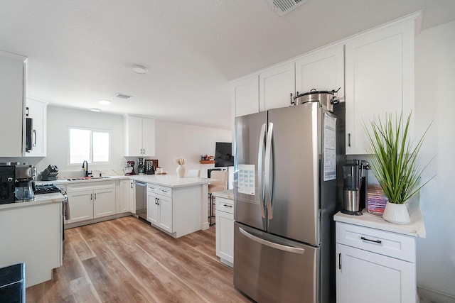 kitchen featuring visible vents, stainless steel appliances, light countertops, white cabinetry, and a sink