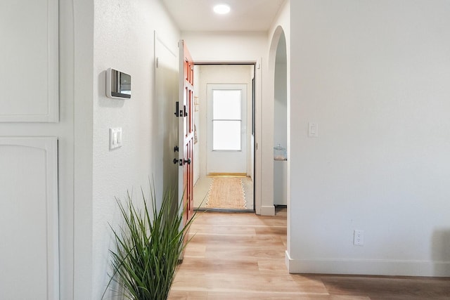 hallway with arched walkways, baseboards, and light wood-style floors