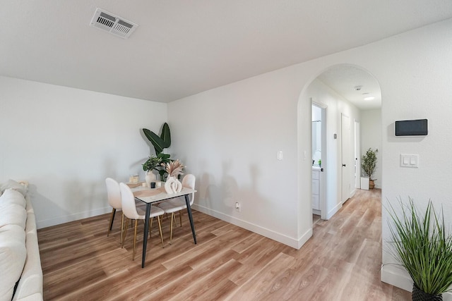 dining space featuring light wood-type flooring, baseboards, visible vents, and arched walkways