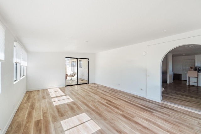 spare room featuring arched walkways, baseboards, and light wood finished floors