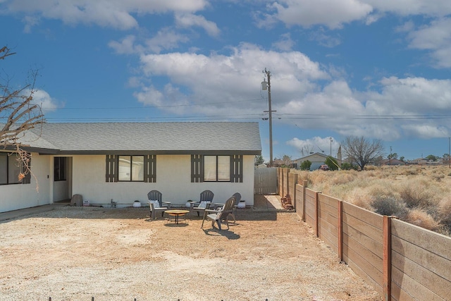 exterior space featuring an outdoor fire pit, roof with shingles, fence private yard, and stucco siding