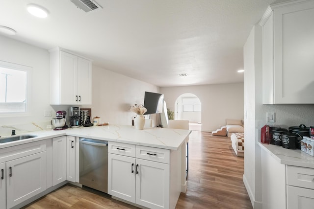 kitchen with arched walkways, a peninsula, visible vents, light wood-style floors, and stainless steel dishwasher