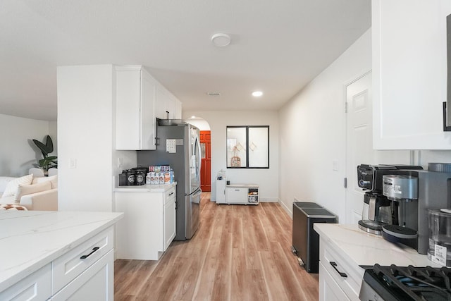 kitchen featuring light wood-style floors, arched walkways, freestanding refrigerator, and white cabinetry