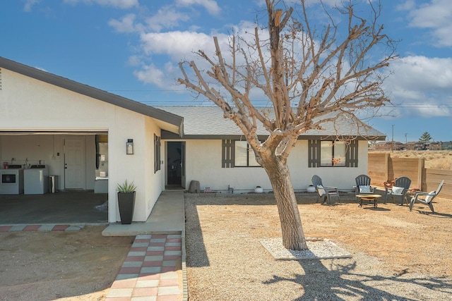 exterior space featuring a fire pit, roof with shingles, an attached garage, washer and dryer, and stucco siding