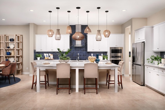 kitchen featuring stainless steel appliances, white cabinetry, an island with sink, hanging light fixtures, and wall chimney range hood