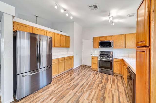 kitchen featuring tile countertops, stainless steel appliances, high vaulted ceiling, and light hardwood / wood-style flooring