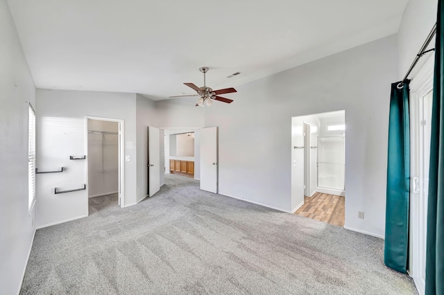 unfurnished bedroom featuring a walk in closet, ensuite bath, light colored carpet, ceiling fan, and a closet