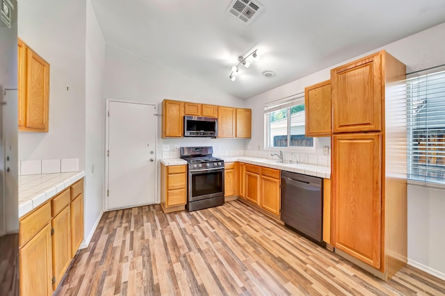 kitchen featuring stainless steel appliances, vaulted ceiling, sink, light hardwood / wood-style flooring, and tile counters