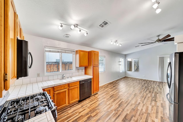 kitchen with tile countertops, lofted ceiling, black dishwasher, range, and stainless steel refrigerator