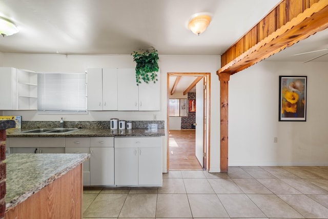 kitchen with sink, white cabinetry, dark stone counters, and light tile patterned flooring