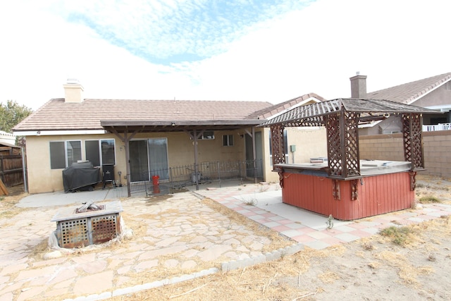 rear view of property with a fire pit, a patio, and a hot tub