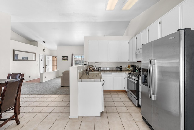 kitchen with a sink, tile countertops, appliances with stainless steel finishes, light tile patterned flooring, and vaulted ceiling