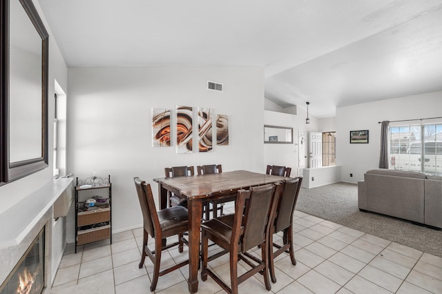 dining area with visible vents, light carpet, a glass covered fireplace, light tile patterned floors, and vaulted ceiling