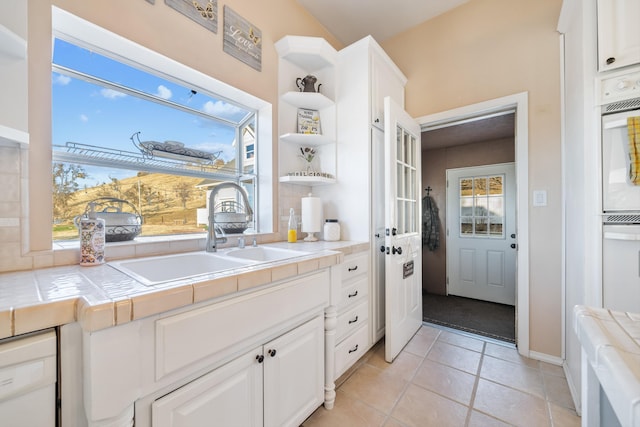 kitchen with light tile patterned floors, tile countertops, sink, and white cabinets