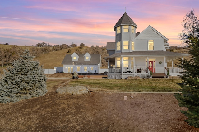 back house at dusk featuring covered porch and a lawn