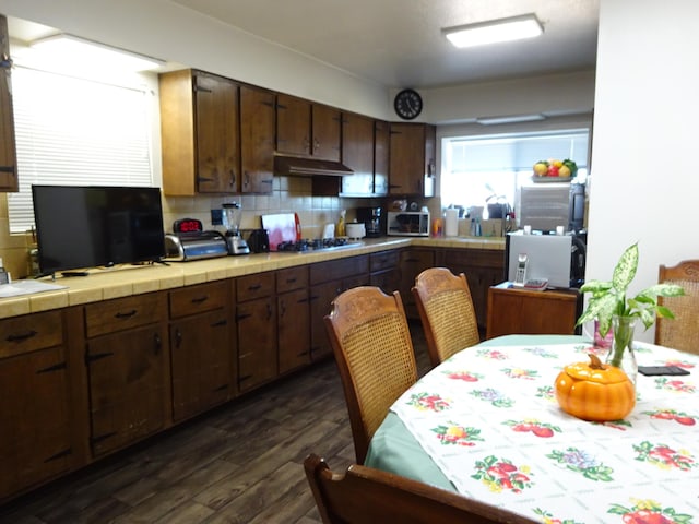 kitchen with tile counters, dark wood-style flooring, under cabinet range hood, gas cooktop, and backsplash