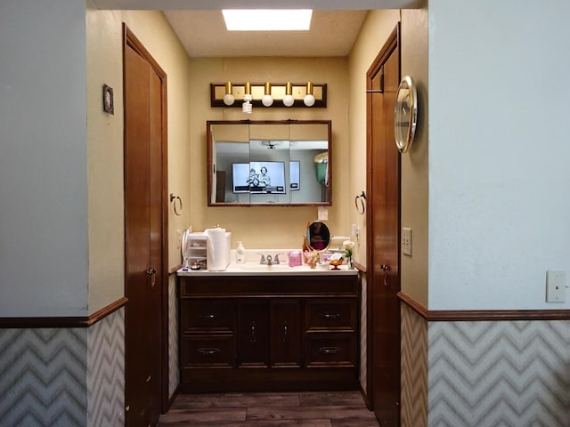 bathroom featuring a skylight, wainscoting, vanity, and wood finished floors