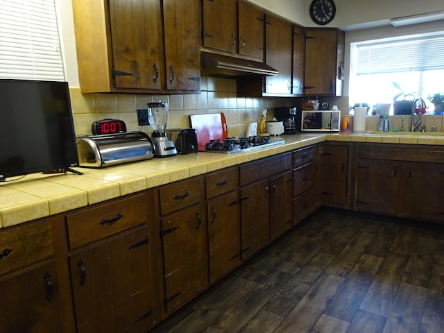 kitchen with tile counters, appliances with stainless steel finishes, dark wood-type flooring, under cabinet range hood, and a sink