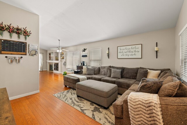 living area featuring a ceiling fan, baseboards, a glass covered fireplace, and light wood-style floors