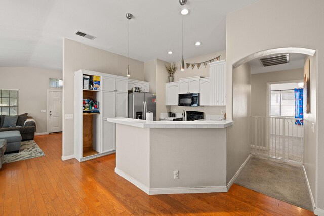 kitchen with black microwave, stainless steel fridge with ice dispenser, arched walkways, tile countertops, and visible vents