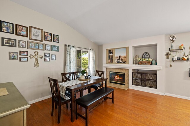 dining space featuring baseboards, lofted ceiling, wood finished floors, and a tile fireplace