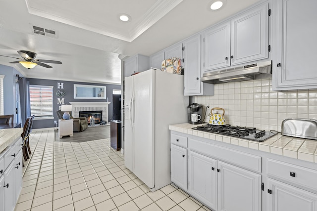 kitchen with tile countertops, white cabinets, white fridge with ice dispenser, a fireplace, and a tray ceiling