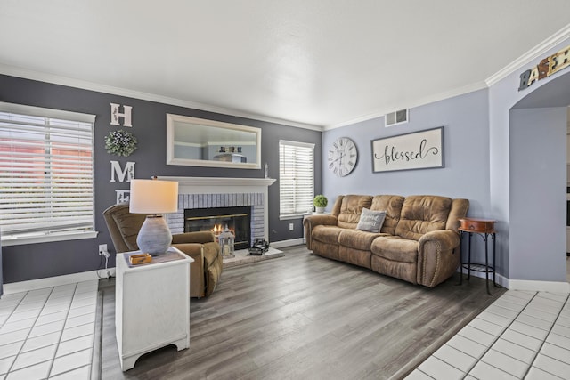 living room featuring wood-type flooring, ornamental molding, and a brick fireplace