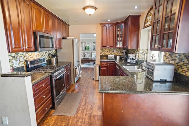 kitchen with appliances with stainless steel finishes, sink, dark hardwood / wood-style flooring, and dark stone counters