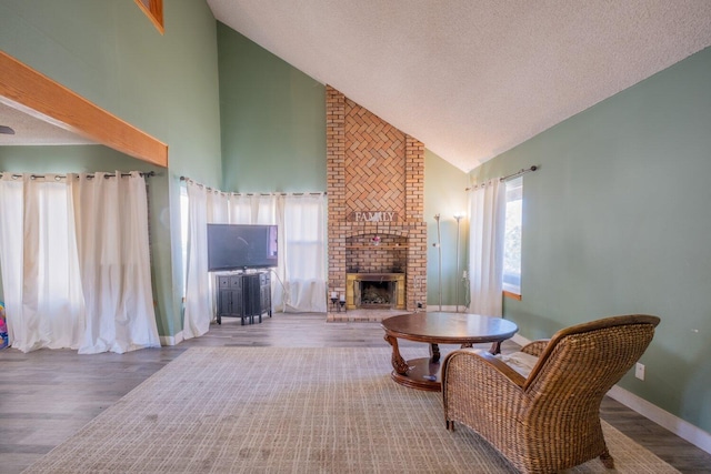 living room with a textured ceiling, high vaulted ceiling, a brick fireplace, and hardwood / wood-style flooring