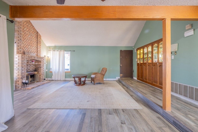 unfurnished room featuring lofted ceiling with beams, hardwood / wood-style flooring, and a brick fireplace